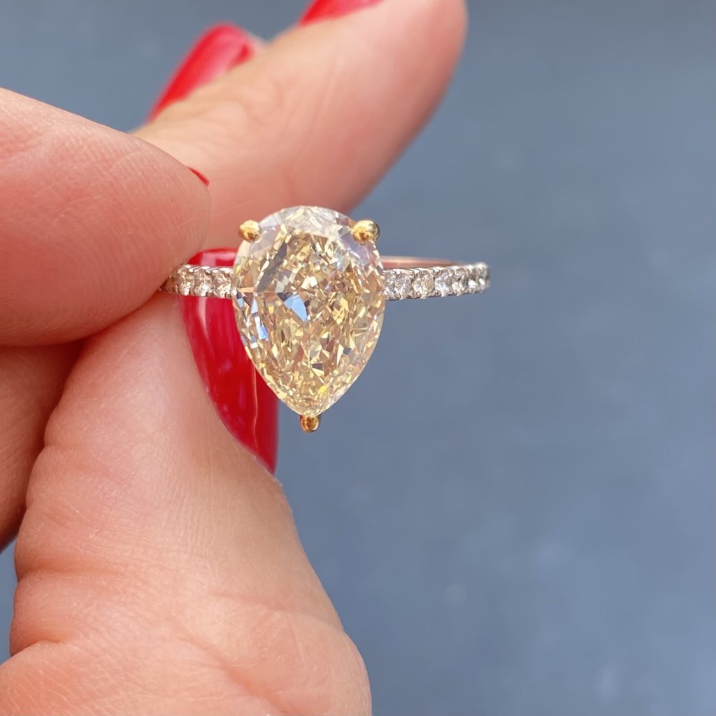 A drop shaped yellow diamond set on a thin diamond band